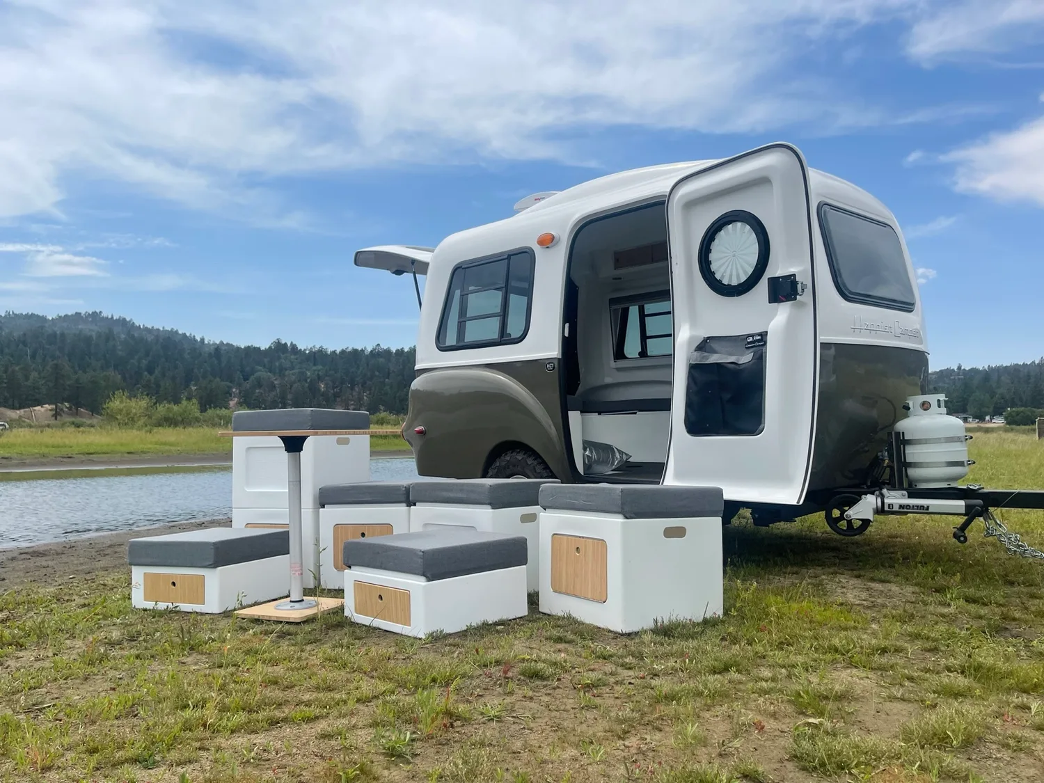 Happier Camper cubes, cushions, and a table arranged outdoors beside the camper